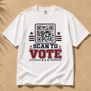 May include: A white short-sleeved t-shirt featuring a graphic design with a black and white QR code above the text SCAN TO VOTE in bold red letters. The design includes blue and red horizontal stripes and small stars in a patriotic color scheme.