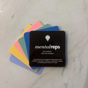 May include: A stack of square waterproof cards with rounded corners. The top card is black with a white lightbulb icon and the text mentalreps, the workout after the workout, and 20 waterproof cards designed to help athletes build confidence.