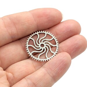 May include: A silver metal gear with a decorative, swirling design. The gear has teeth around the outer edge.
