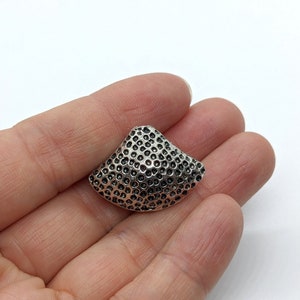 Puede incluir: Un colgante de metal plateado con un diseño texturizado en forma de panal. El colgante tiene forma de semicírculo.