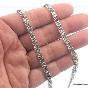 May include: A silver chain necklace with a unique, intricate design. The chain is made of small, linked loops that create a delicate and stylish look.