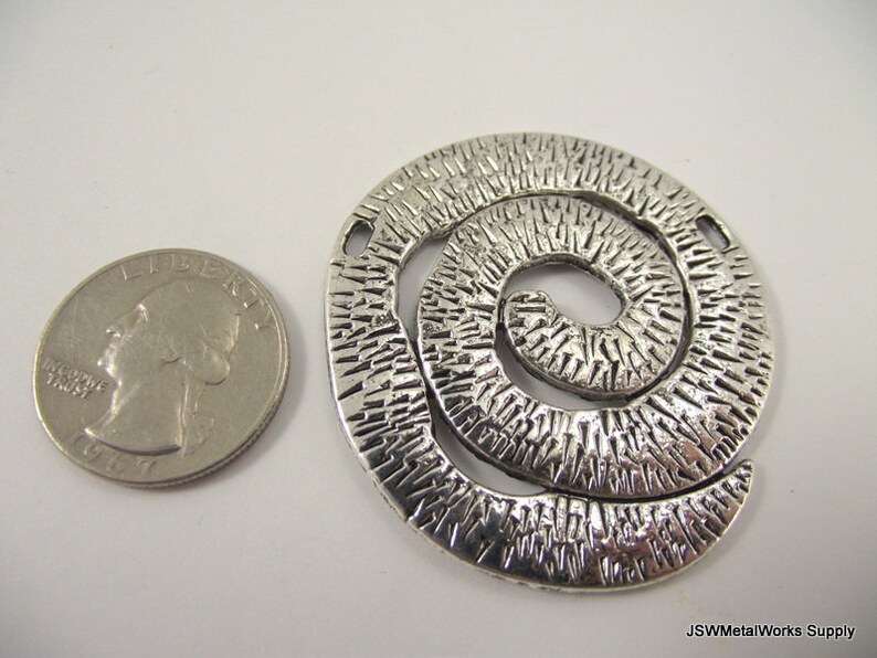 K&ouml;nnte beinhalten: Silberner Metalls Anh&auml;nger mit einem strukturierten Spiralendesign. Der Anh&auml;nger ist etwa so gro&szlig; wie eine US-amerikanische 25-Cent-M&uuml;nze.