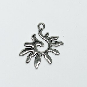 May include: Silver charm in the shape of a stylised sun with a swirl in the centre.
