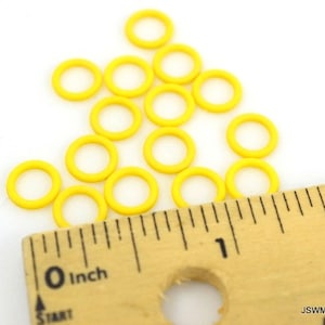 May include: A close-up of a ruler measuring a pile of yellow jump rings. The ruler is marked in inches.