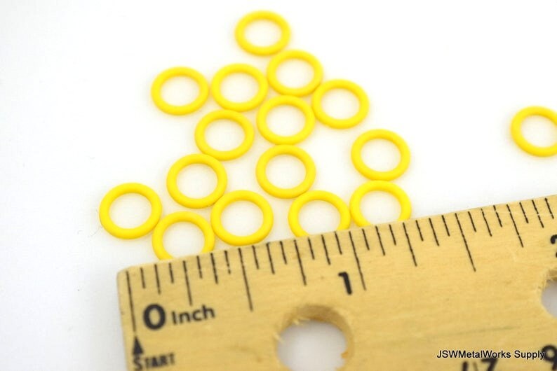 May include: A close-up of a ruler measuring a pile of yellow jump rings. The ruler is marked in inches.