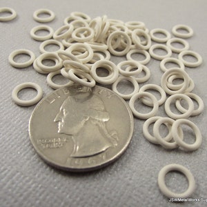 May include: A pile of white metal jump rings, approximately 1/2 inch in diameter, next to a US quarter for size comparison.