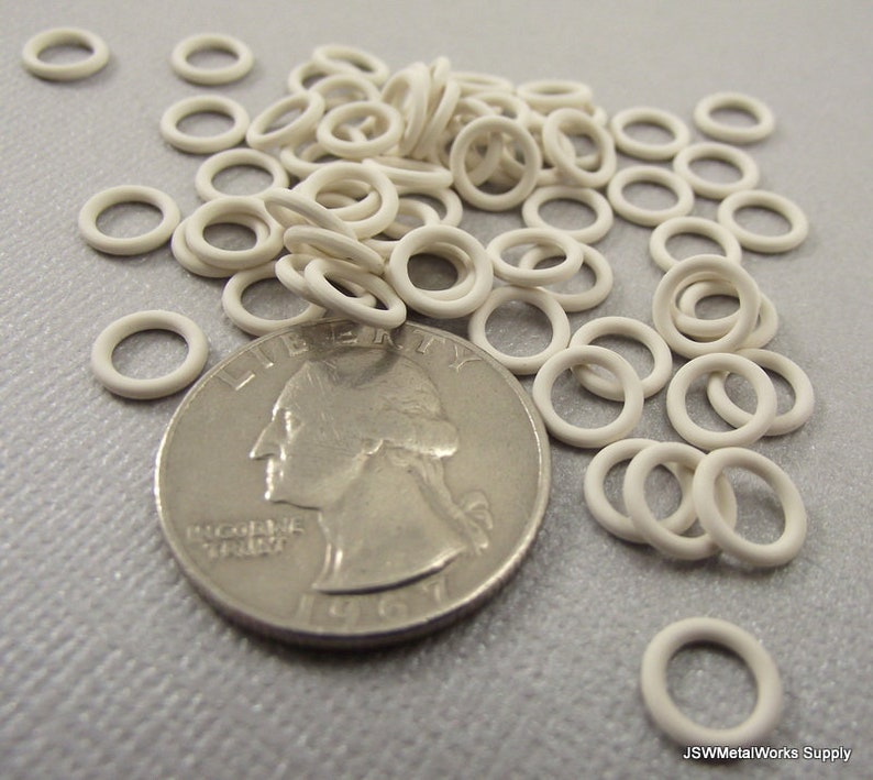 May include: A pile of white metal jump rings, approximately 1/2 inch in diameter, next to a US quarter for size comparison.