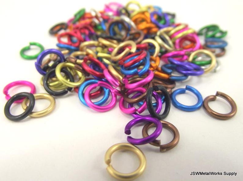 May include: A large assortment of colorful metal jump rings. The rings are made of aluminum and come in a variety of sizes and colors, including gold, silver, black, red, blue, green, purple, and pink.
