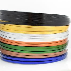 May include: A stack of colorful metal trim, including black, gold, silver, orange, green, copper, and blue.