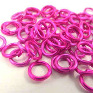 May include: A pile of bright pink metal jump rings. The rings are small and round, and they are perfect for jewelry making or other crafts.