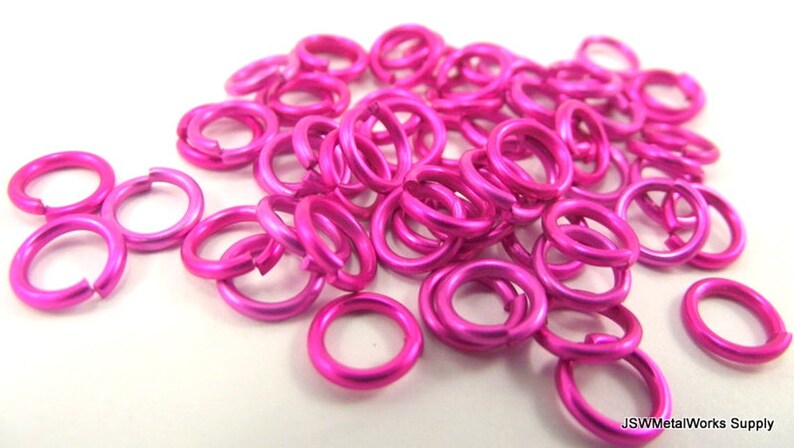 May include: A pile of bright pink metal jump rings. The rings are small and round, and they are perfect for jewelry making or other crafts.