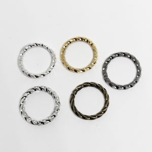 May include: Five twisted metal rings in different colors: silver, gold, black, bronze, and silver. The rings are all the same size and are arranged in a circle.