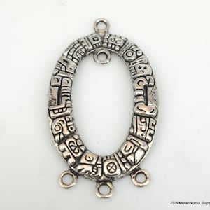 May include: Oval-shaped silver-toned metal pendant with intricate engraved designs. The pendant features a central oval opening and multiple small loops for attachment. The surface is detailed with repeating patterns and symbols.