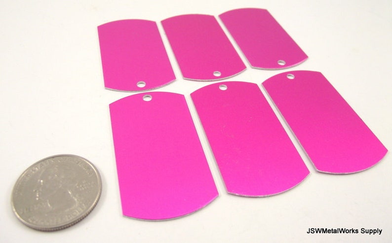May include: Six blank, pink, metal dog tags with rounded edges and a hole at the top. The tags are about the size of a US quarter.