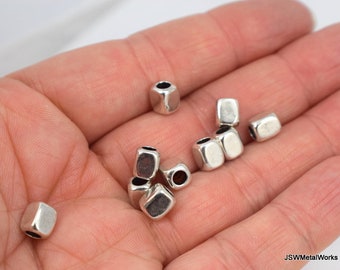 May include: A close-up of silver metal square beads with a hole in the center. The beads are in a hand, ready to be used for jewelry making.
