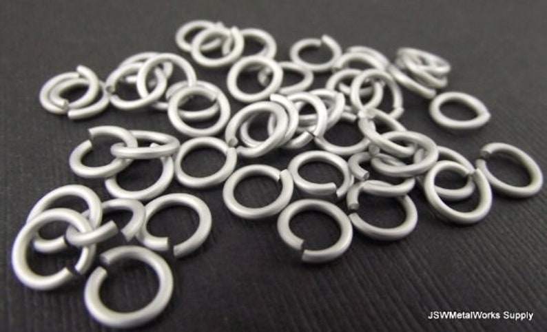 May include: A pile of silver jump rings, a type of metal ring used in jewelry making and crafting.