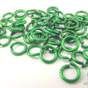 May include: A pile of small, green metal jump rings. The rings are about 6mm in diameter and are made of aluminum.