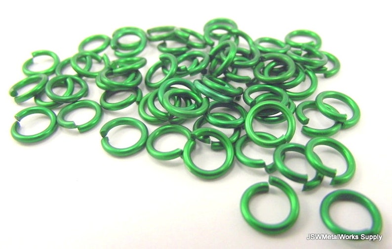 May include: A pile of small, green metal jump rings. The rings are about 6mm in diameter and are made of aluminum.