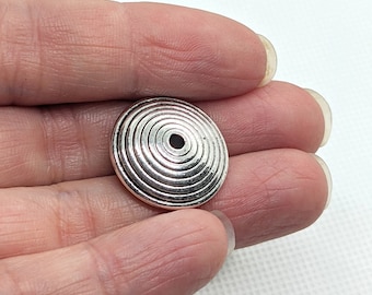 May include: Silver metal bead with a circular design featuring concentric circles. The bead has a hole in the center.