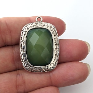 Puede incluir: Un colgante de plata con una piedra de vidrio facetada verde engastada en un marco texturizado.