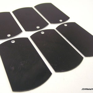 May include: Six black metal dog tags with rounded edges and a hole for a ring. The tags are blank and ready for engraving.