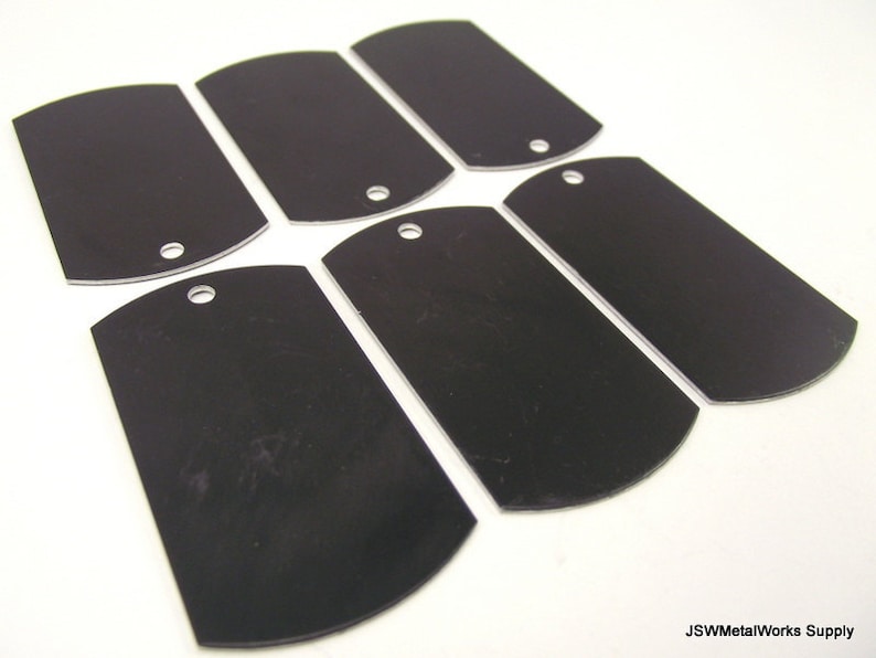 May include: Six black metal dog tags with rounded edges and a hole for a ring. The tags are blank and ready for engraving.