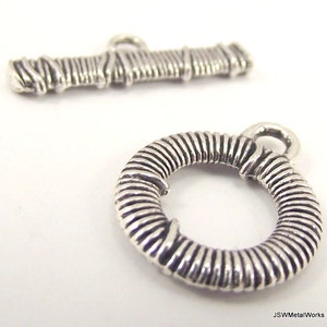 May include: Silver tone metal toggle clasp with a twisted wire design. The clasp has a round ring and a rectangular bar.