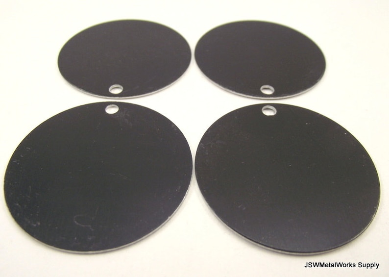 Op de afbeelding: Vier ronde zwarte metalen schijven met een gat in het midden. De schijven zijn ongeveer 5 cm in diameter.