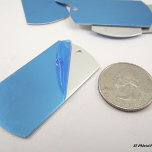 May include: A close-up of a silver metal dog tag with a blue protective film on one side. The dog tag is about the size of a US quarter.