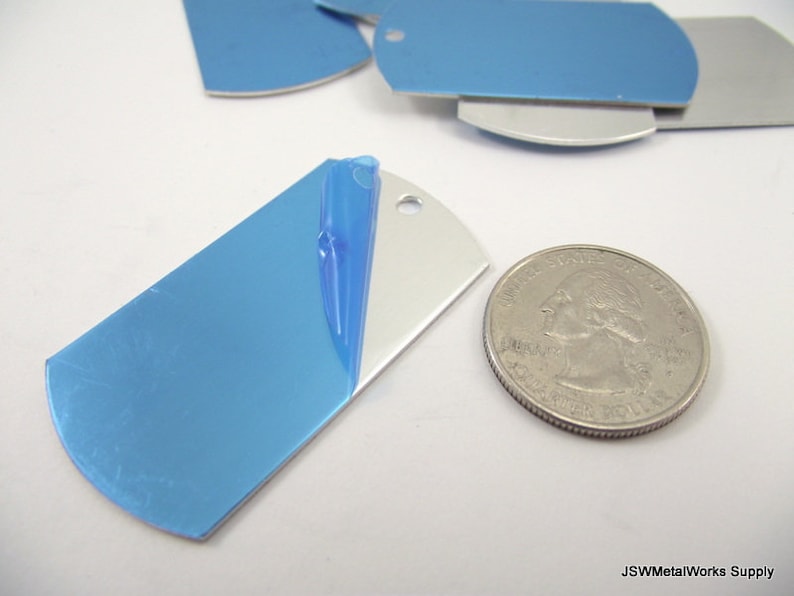 May include: A close-up of a silver metal dog tag with a blue protective film on one side. The dog tag is about the size of a US quarter.