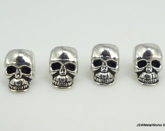 May include: Four silver skull-shaped beads. The beads are about 1 inch in diameter and have a detailed skull design.