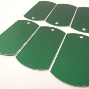May include: Six blank, green metal dog tags with rounded edges and a hole punched in the top. The tags are arranged in a semi-circle pattern.