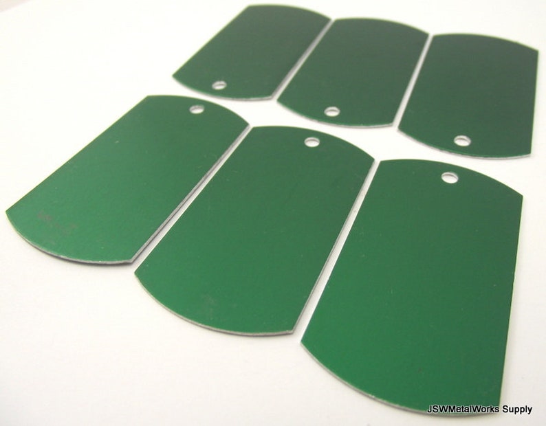 May include: Six blank, green metal dog tags with rounded edges and a hole punched in the top. The tags are arranged in a semi-circle pattern.