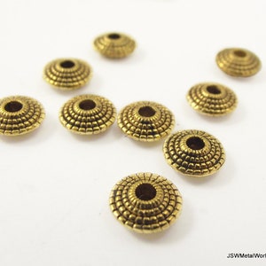 Pode incluir: Um grupo de oito tampas de contas de metal dourado com um design decorativo e texturizado. As tampas são redondas e têm um pequeno furo no centro.