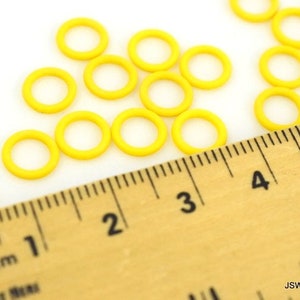 May include: A close-up of a ruler measuring yellow jump rings. The ruler is marked in centimeters and inches. The jump rings are scattered on a white surface.