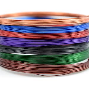 Puede incluir: Una pila de carretes de alambre de cobre de colores en tonos cobre, azul, rojo, morado, negro, verde y marrón.