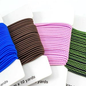 Könnte beinhalten: Vier Spulen elastischer Schnur in verschiedenen Farben: Blau, Braun, Pink und Grün mit schwarzen Punkten. Jede Spule ist mit dem Text "10 Yards" beschriftet.