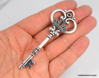 May include: A silver-toned ornate key with a crown-shaped top and a detailed design. The key is held in a hand, showcasing its size and intricate details.