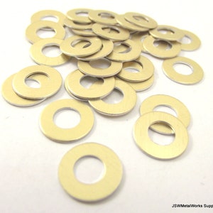 May include: A pile of 25 gold-coloured metal washers. The washers are round with a hole in the centre. The washers are scattered on a white surface.