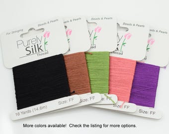 Op de afbeelding: Spoelen Purely Silk-garen in verschillende kleuren: zwart, bruin, groen, roze en paars. Elke spoel is gemarkeerd met "16 Yards (14,6 m)" en "Size: FF". De verpakking bevat de tekst "Beads & Pearls" en "For Stringing".