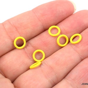 May include: A close-up of six yellow rubber o-rings on a hand. The o-rings are small and round.