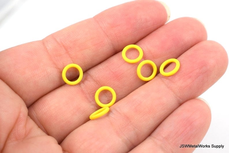 May include: A close-up of six yellow rubber o-rings on a hand. The o-rings are small and round.