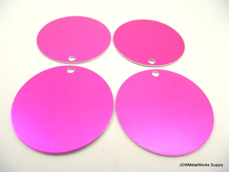 Op de afbeelding: Vier ronde, roze metalen schijven met een gat in het midden. De schijven zijn glad en hebben een lichte glans.