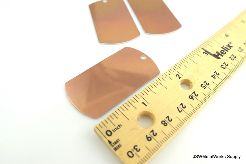 May include: Three copper-colored metal dog tags with rounded edges. The largest tag is 1 inch wide and 1.5 inches long. The tags have a hole at the top for attaching a chain or lanyard.