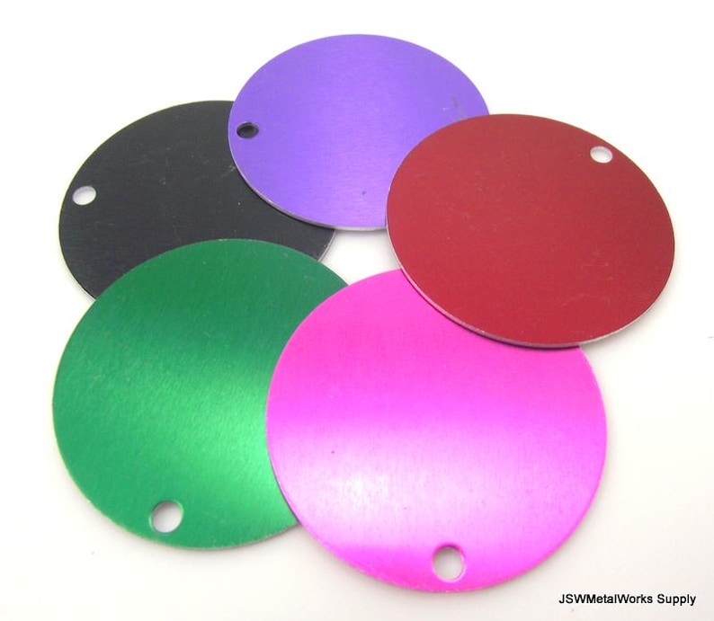 Op de afbeelding: Vijf ronde metalen schijven in verschillende kleuren: zwart, paars, rood, groen en roze. Elke schijf heeft een klein gaatje in het midden.