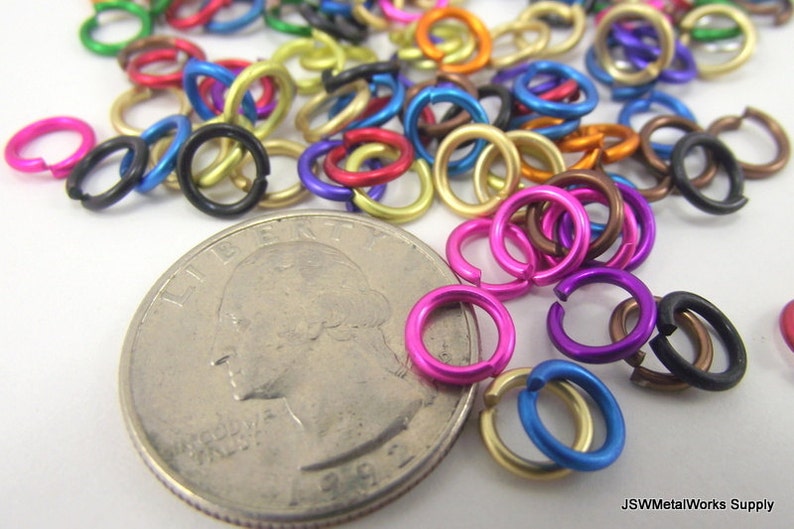 May include: A variety of colorful metal jump rings in different sizes, next to a US quarter for scale. The jump rings are used for jewelry making and crafting.