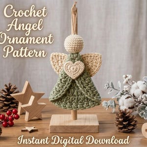 Puede incluir: Un adorno de ángel de ganchillo con cabeza redonda color crema, vestido verde salvia y alas color crema con un corazón central. El adorno cuelga de un soporte de madera. El texto dice: Crochet Angel Ornament Pattern e Instant Digital Download.
