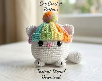 Pode incluir: Um brinquedo de gato em crochê branco usando um gorro com as cores do arco-íris e um pompom a condizer no topo. O gato tem olhos pretos, um pequeno nariz cor-de-rosa e patas brancas. O texto Cat Crochet Pattern e Instant Digital Download aparece.