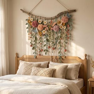 May include: A wall hanging featuring a curved piece of driftwood adorned with crocheted flowers in shades of pink, yellow, and white, along with green crocheted leaves, vines, and small butterflies, suspended by a simple rope cord.