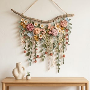 May include: A wall hanging featuring crocheted flowers, leaves, and butterflies in shades of pink, yellow, green, and blue, attached to a natural wooden branch with a jute string for suspension, showcasing intricate yarn textures and floral details.